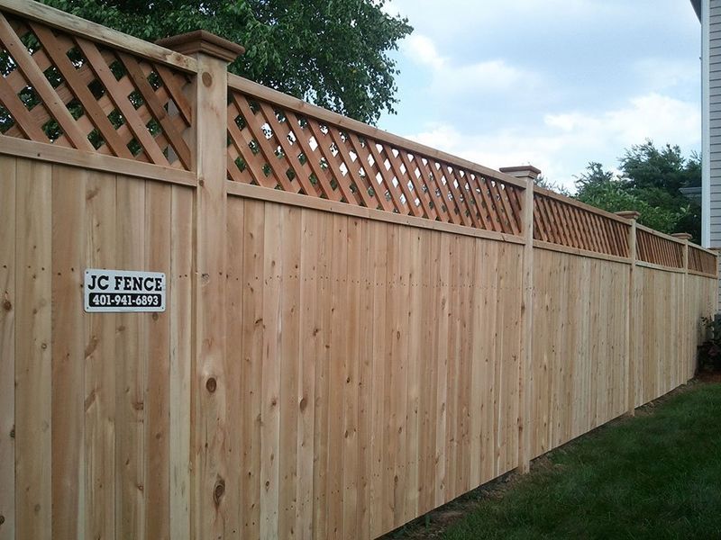 A wooden fence made of vertical boards with a decorative lattice top, featuring a JC Fence company sign.