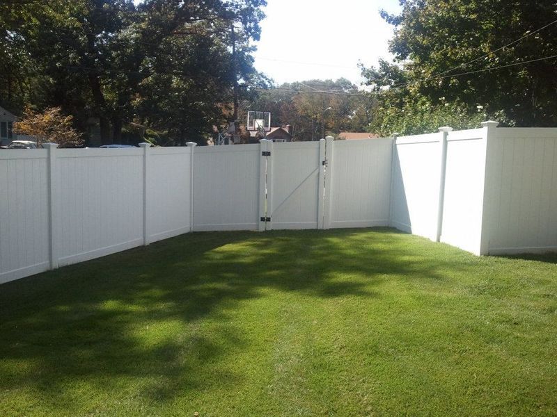 A green backyard lawn enclosed by a white vinyl privacy fence with a central gate.