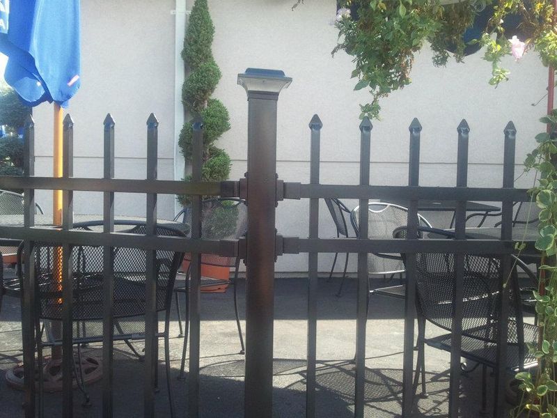 A black metal picket fence in front of an outdoor patio area with tables and chairs.