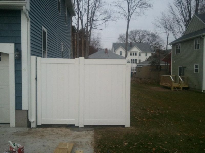 A white privacy fence stands between two residential houses on a suburban lot.