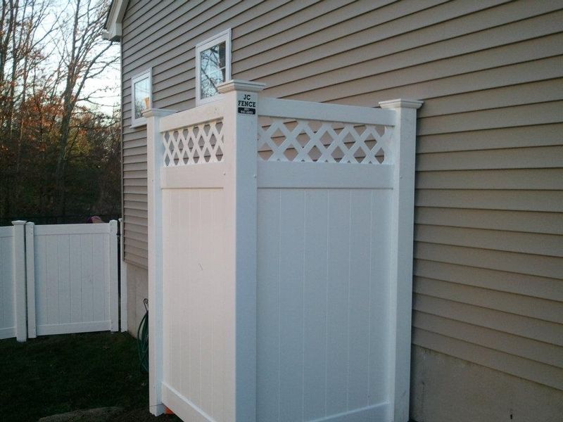 A white vinyl privacy screen with a lattice top section stands against the beige siding of a house.