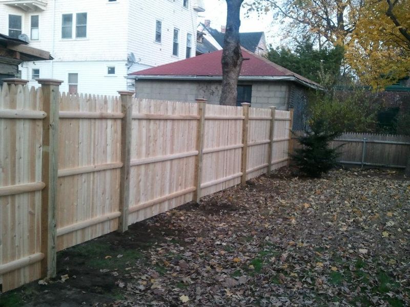 A newly installed wooden privacy fence running along the edge of a backyard covered in fallen autumn leaves.