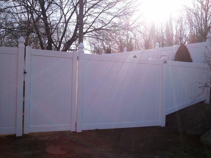 White vinyl privacy fence and gate outdoors on a sunny day with trees in the background.