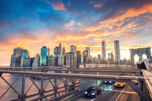 Brooklyn Bridge at sunset with NYC skyline, cars, and vibrant sky.