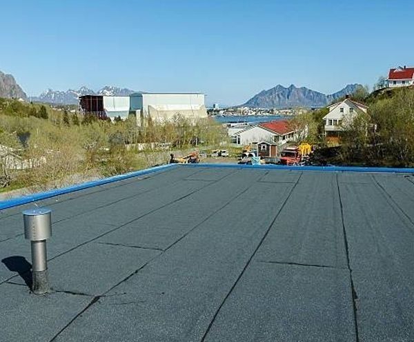 Flat rooftop with a cityscape and mountains in the background under a clear blue sky.