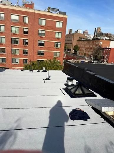View of a rooftop with a shadow. Brick building and other structures in the background.