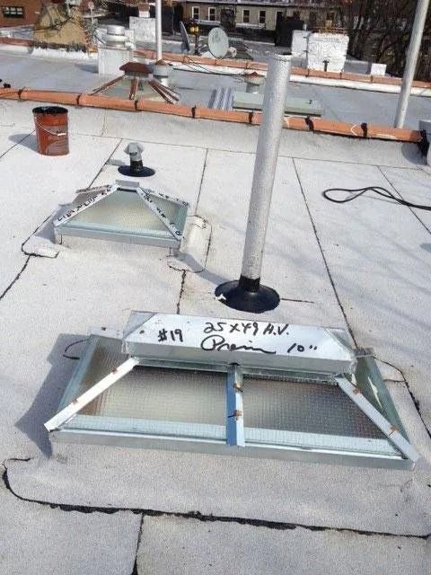 Flat rooftop with two skylights, vent pipe, and a paint can.