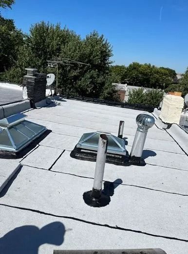 White flat roof with skylights, vents, and a chimney under a clear blue sky.