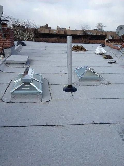 A flat, gray rooftop with two skylights, a vent pipe, and other rooftop equipment.