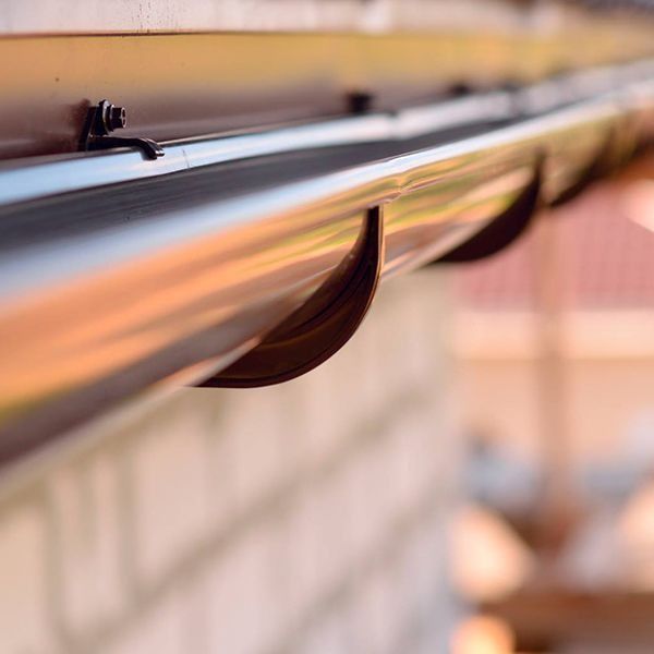 Brown rain gutter with curved leaf guards installed along the edge of a house.