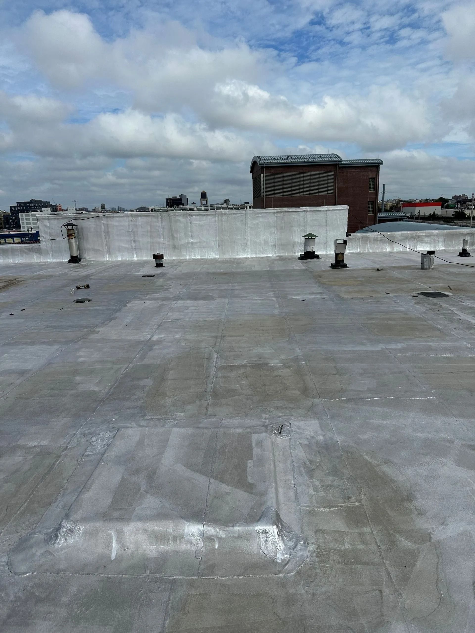 Flat rooftop with vents and a brick building in the background under a cloudy sky.