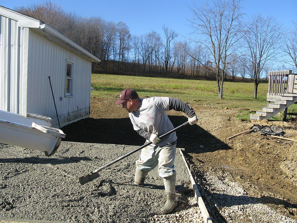 A man is shoveling concrete in front of a white building