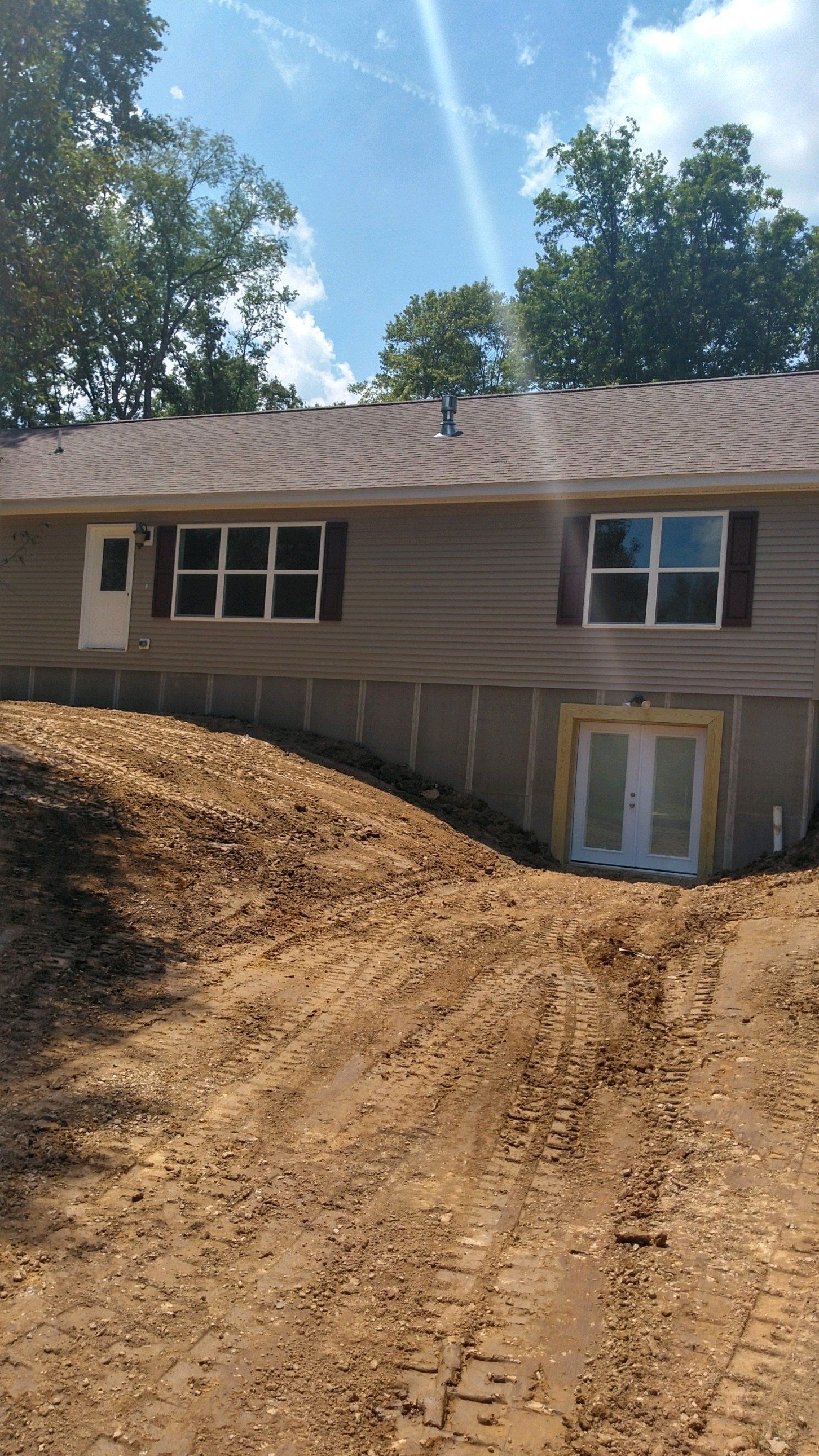 A house sits on top of a dirt hill next to a dirt road