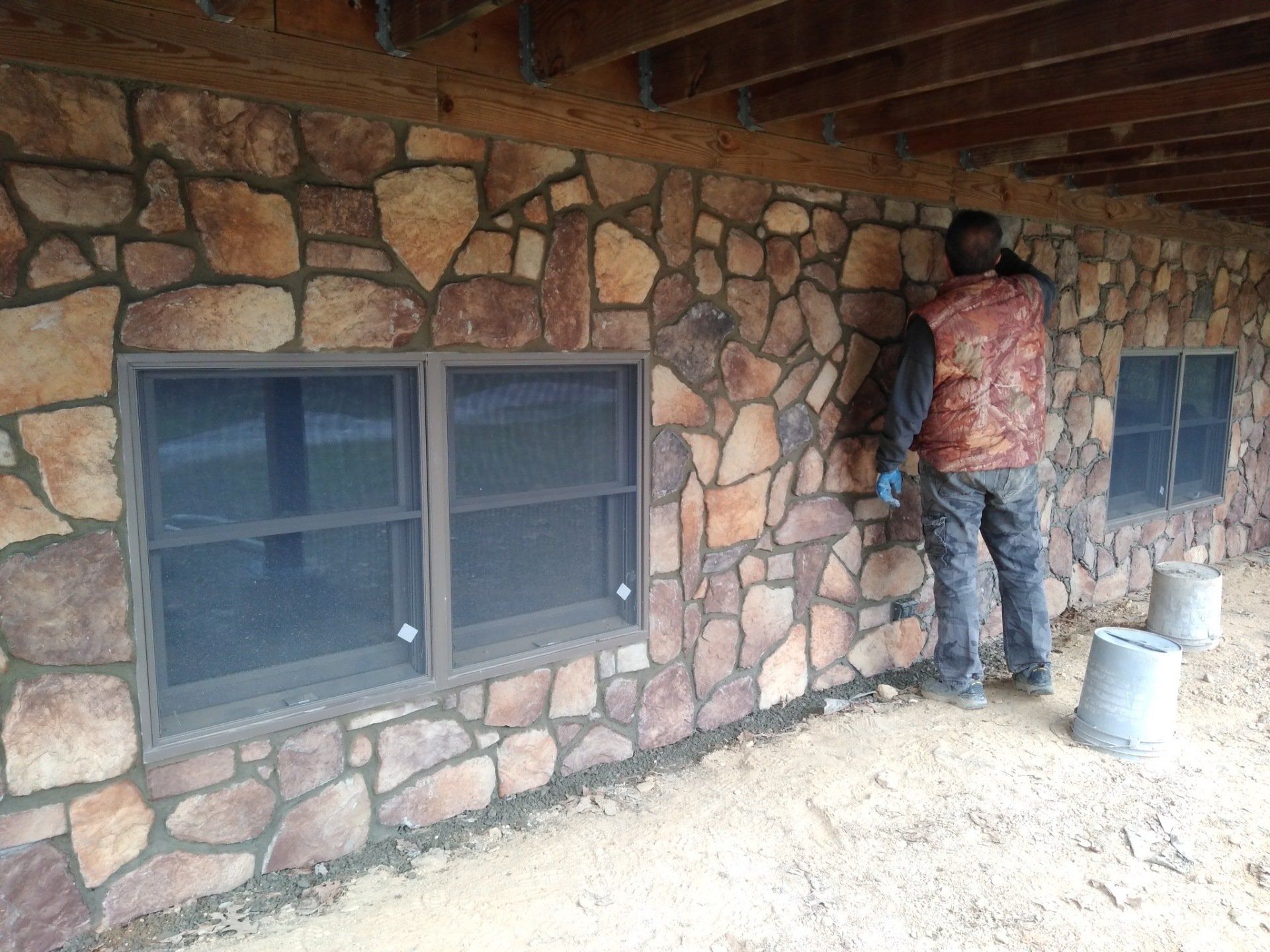 A man is standing in front of a stone wall with two windows