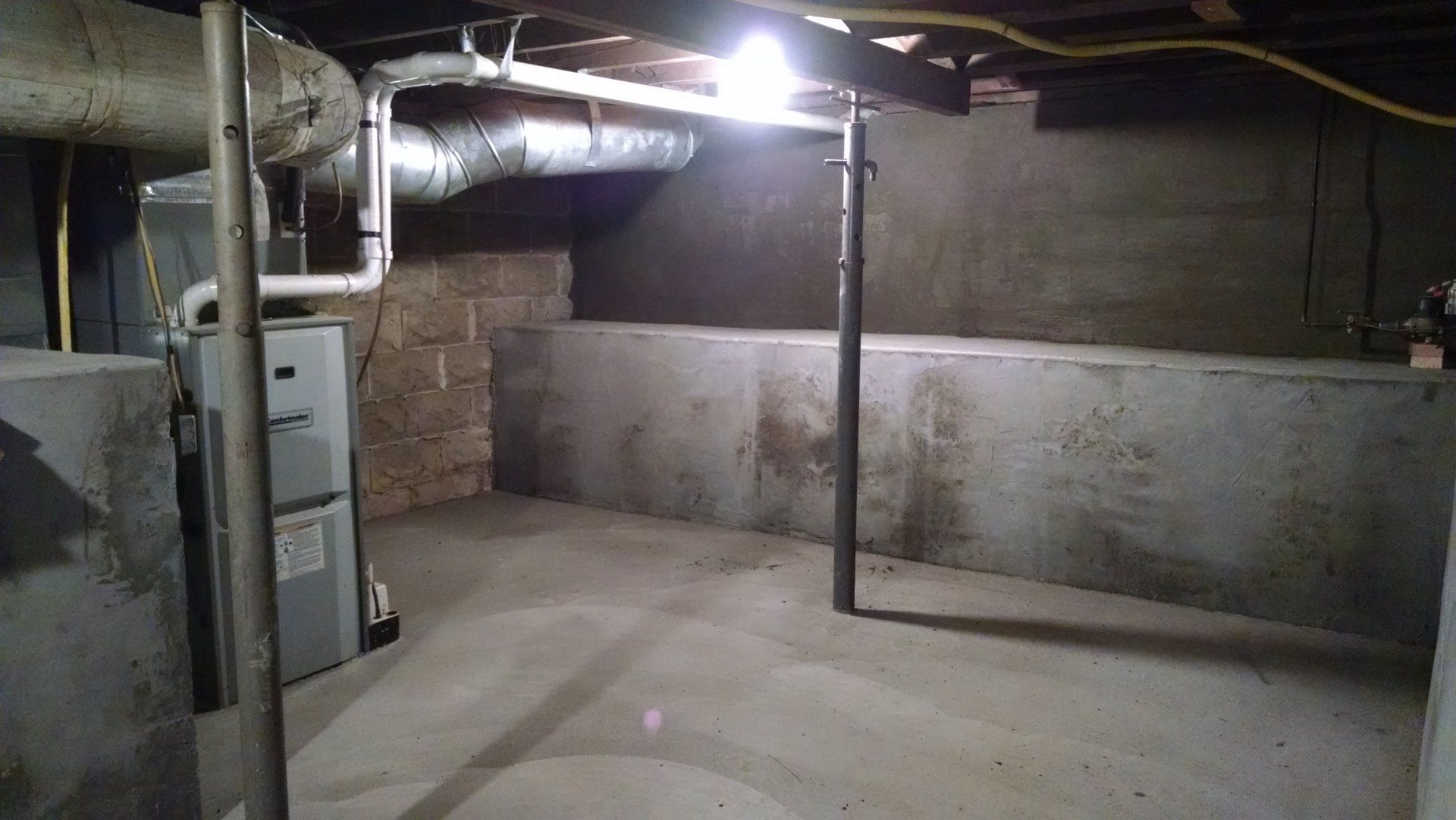 An empty basement with a furnace and a light on