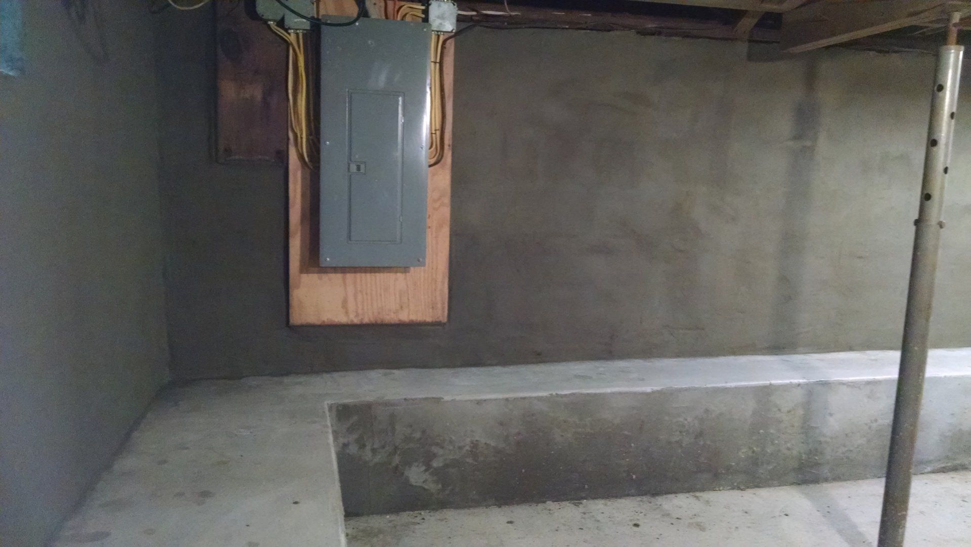 A basement with a concrete floor and a electrical box on the wall