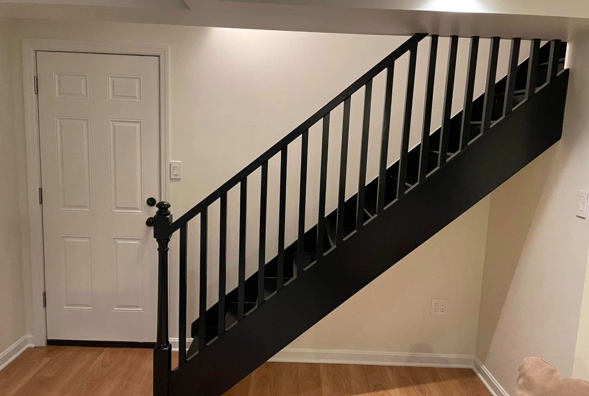 Black staircase with matching railing, leading up. White door on the left.