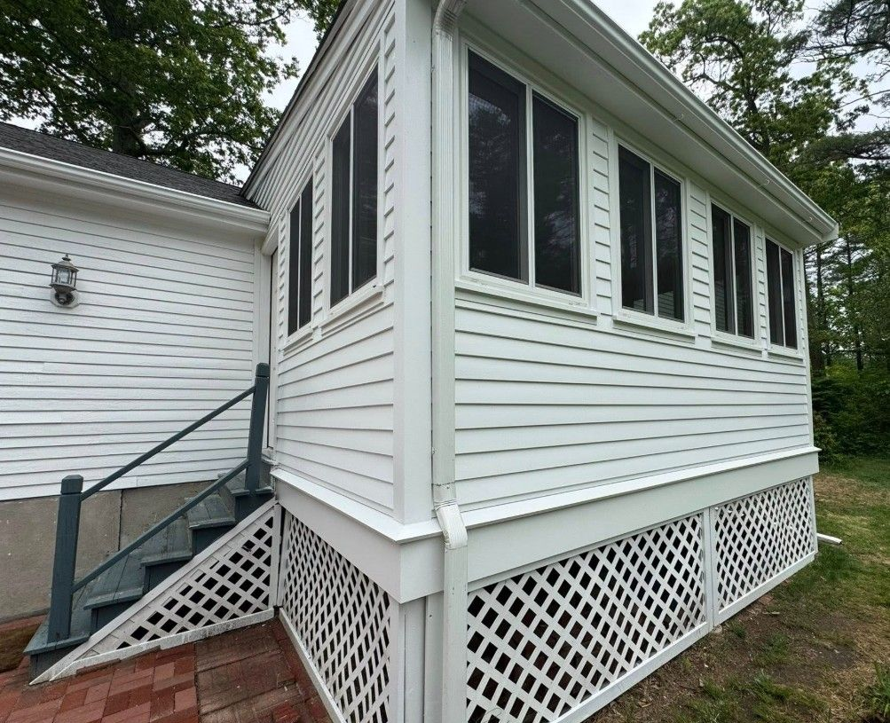 White screened-in porch with lattice skirting, attached to a house with brick steps.