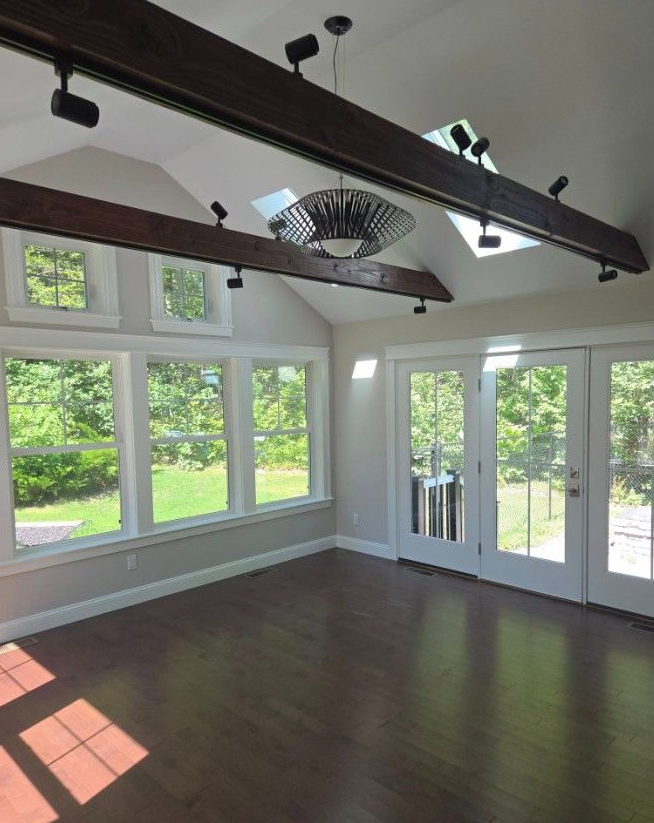 Sunroom with dark beams, skylights, and windows overlooking a green landscape.