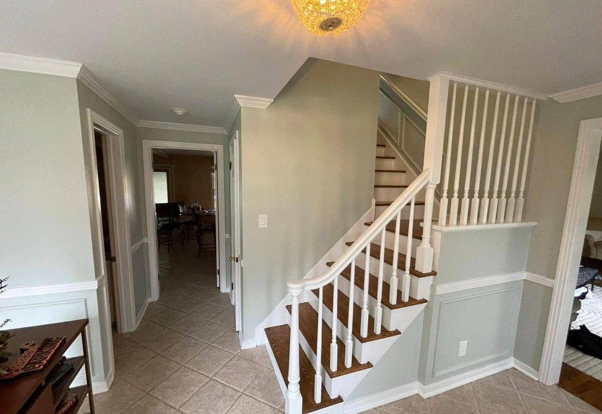 Entryway with stairs, hallway, and doors. White trim on walls, brown stairs, light green walls.
