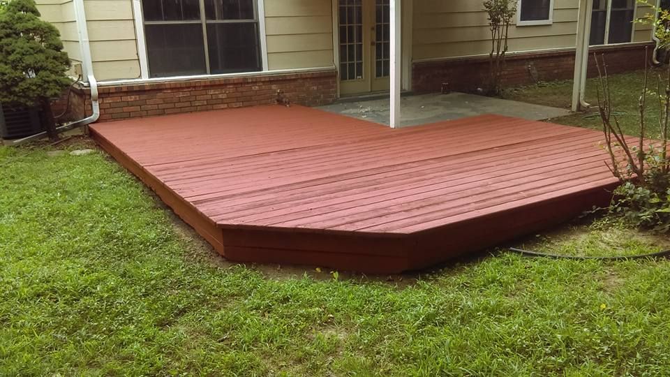 A red wooden deck attached to the back of a house, surrounded by a green lawn.