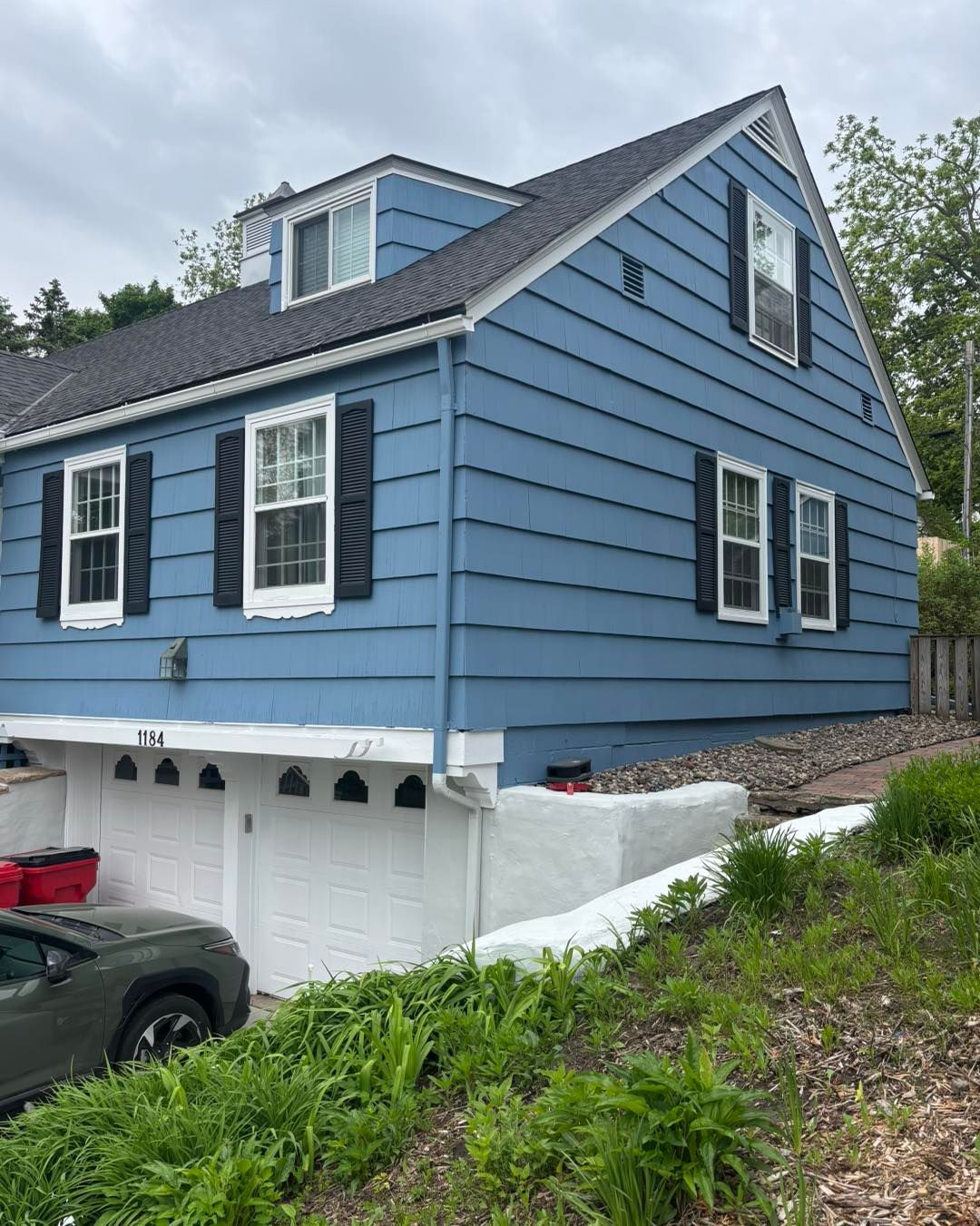 Blue house with dark blue shutters and white garage doors.