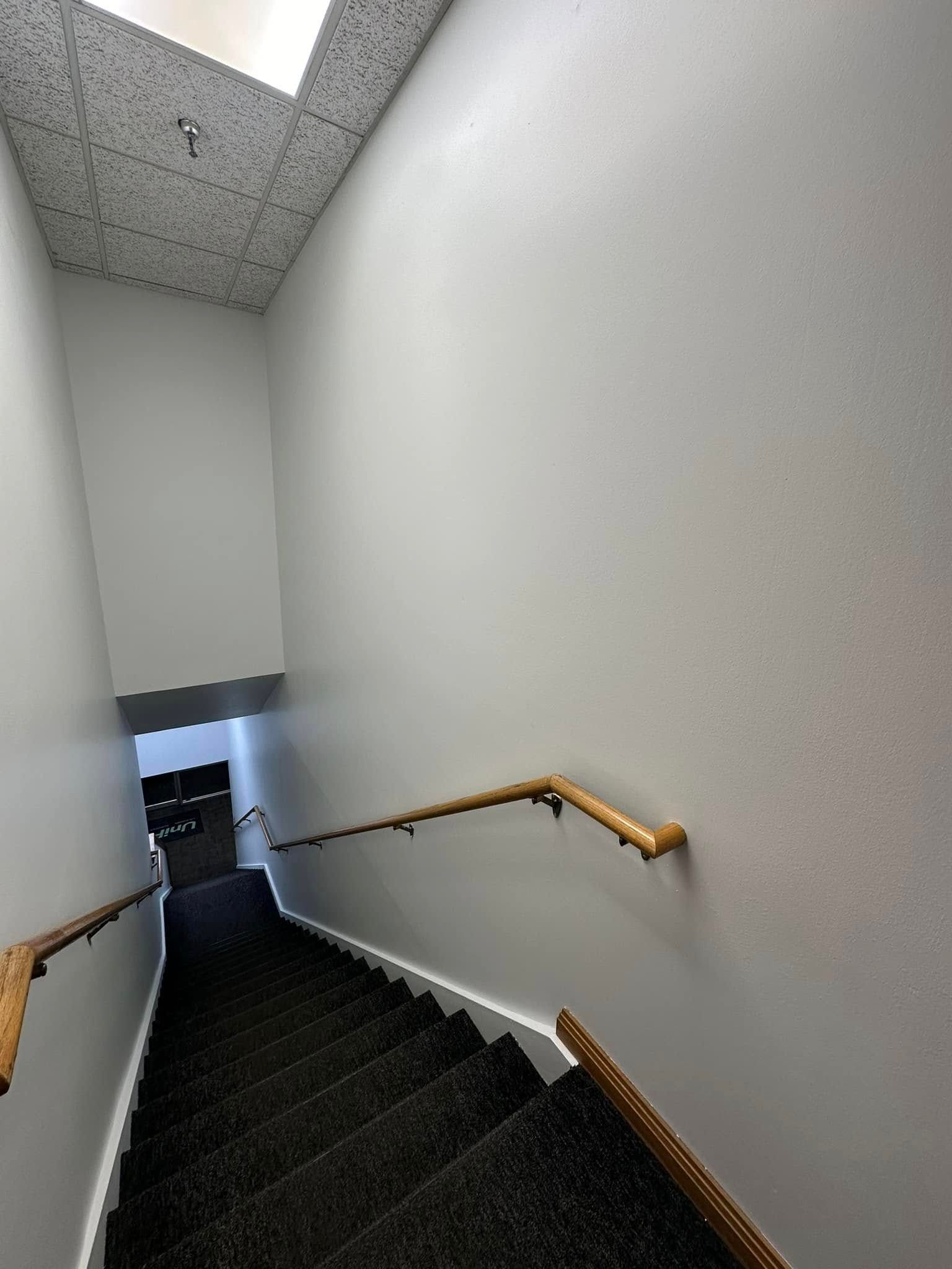 Commercial building stairwell painted with white walls, brown railing and dark carpet in Ankeny, Iowa.