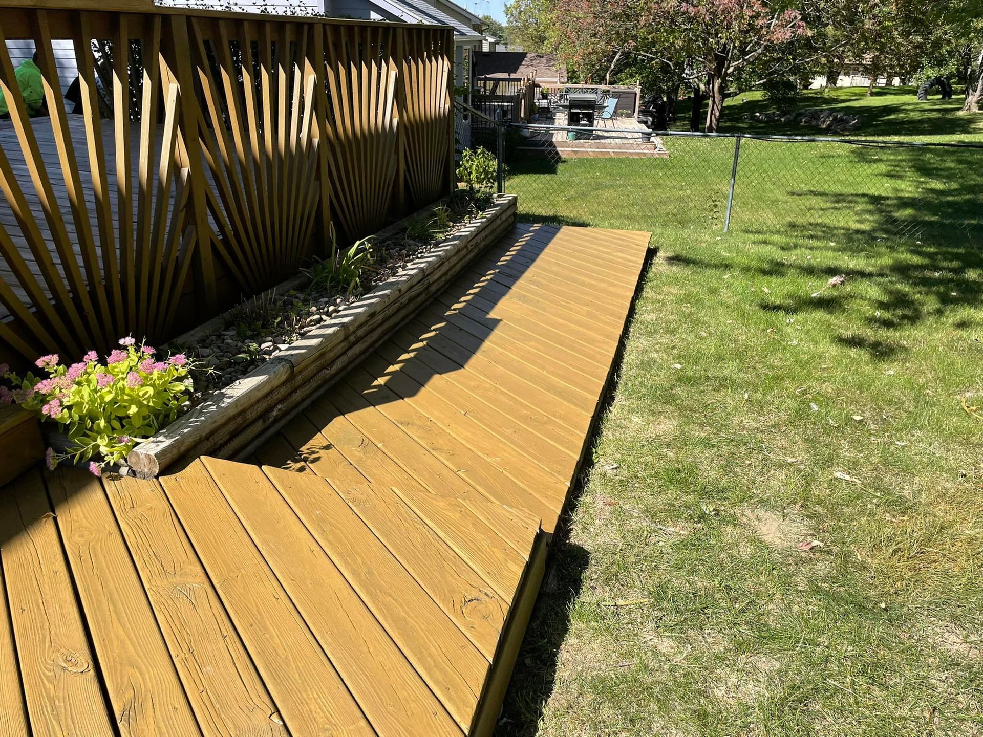 Wooden deck with a flower bed and sloped walkway in a sunny backyard.
