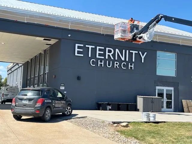 Exterior of Eternity Church building with signage being installed; a grey SUV parked in front.