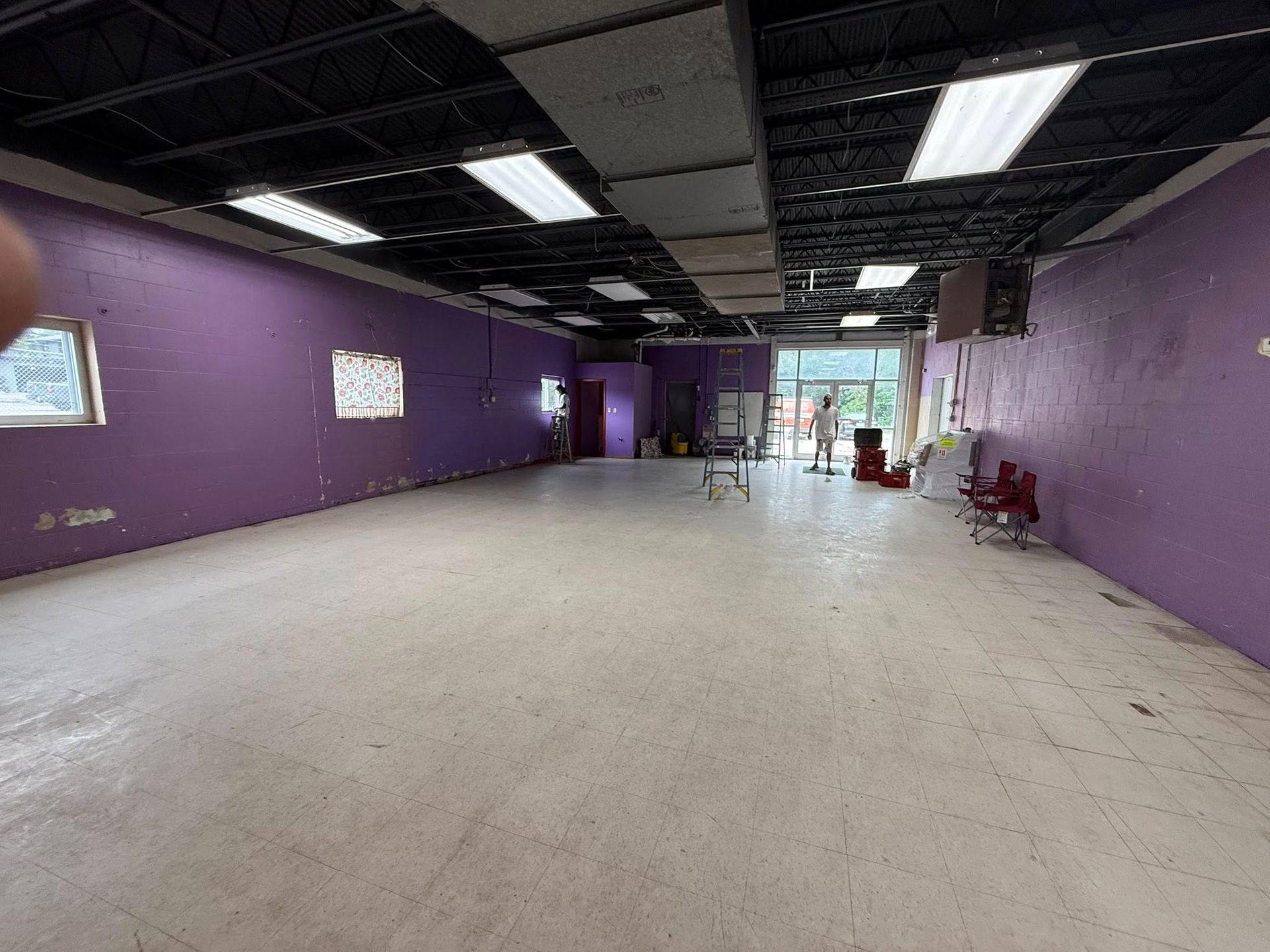 Empty room with purple walls, fluorescent lights, and a white floor.