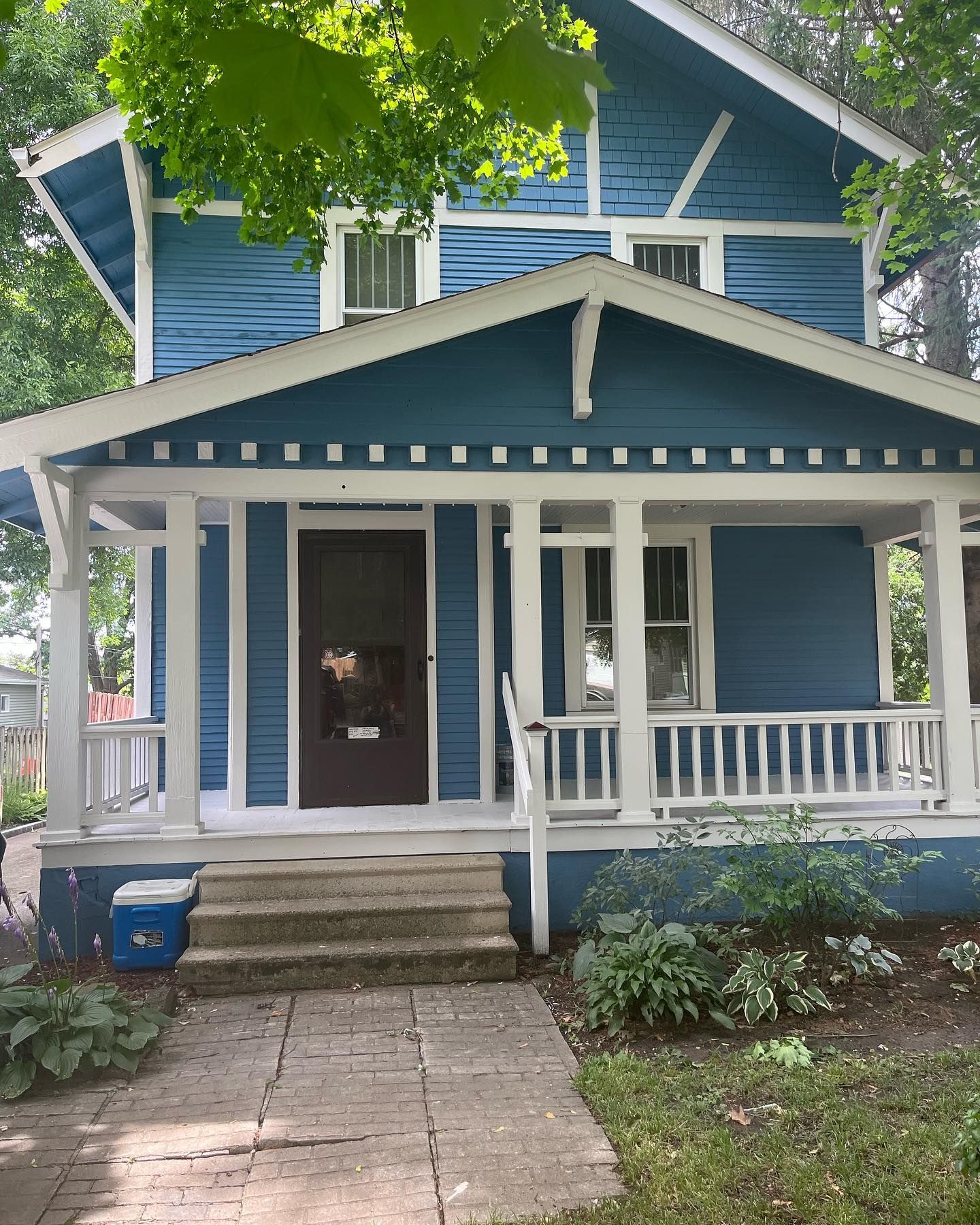Blue house with white porch, steps, and trim, shaded by trees.