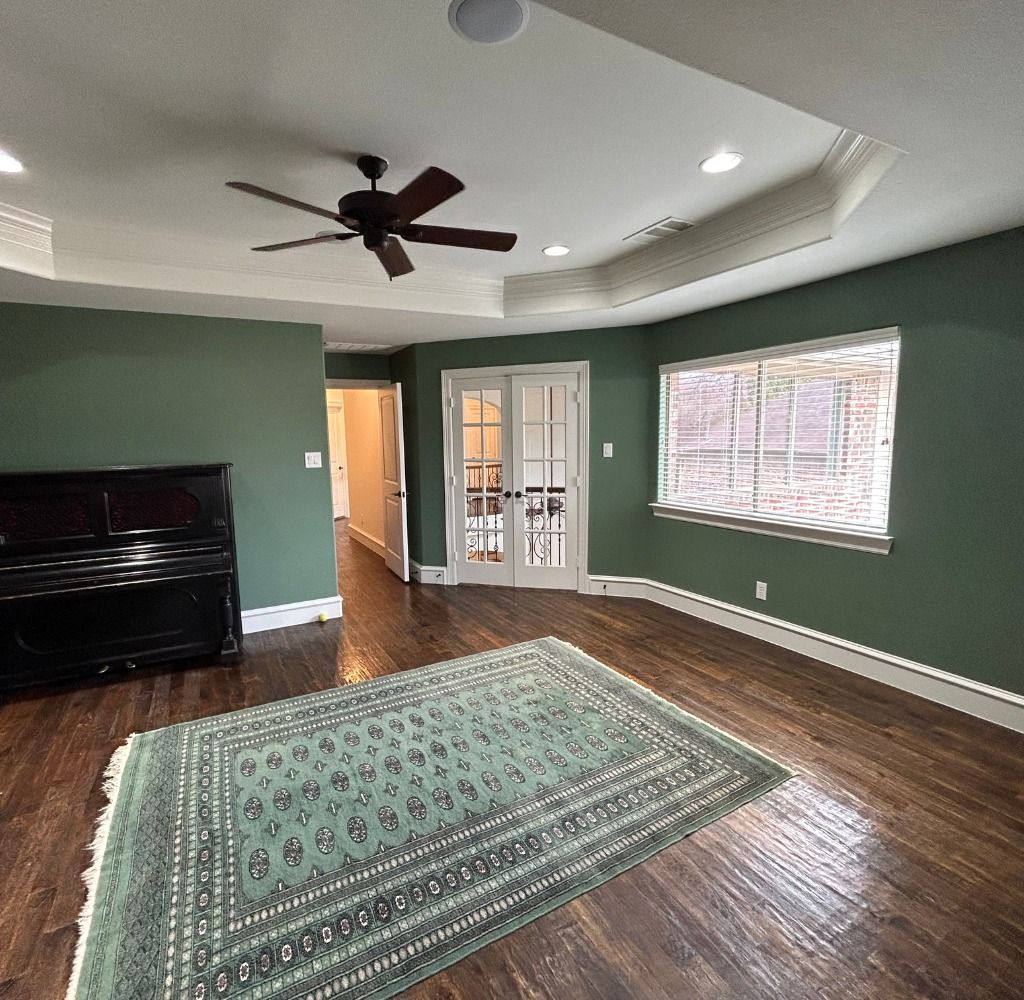 Room with green walls, dark wood floors, and a rug. It has a piano, french doors, and a window.