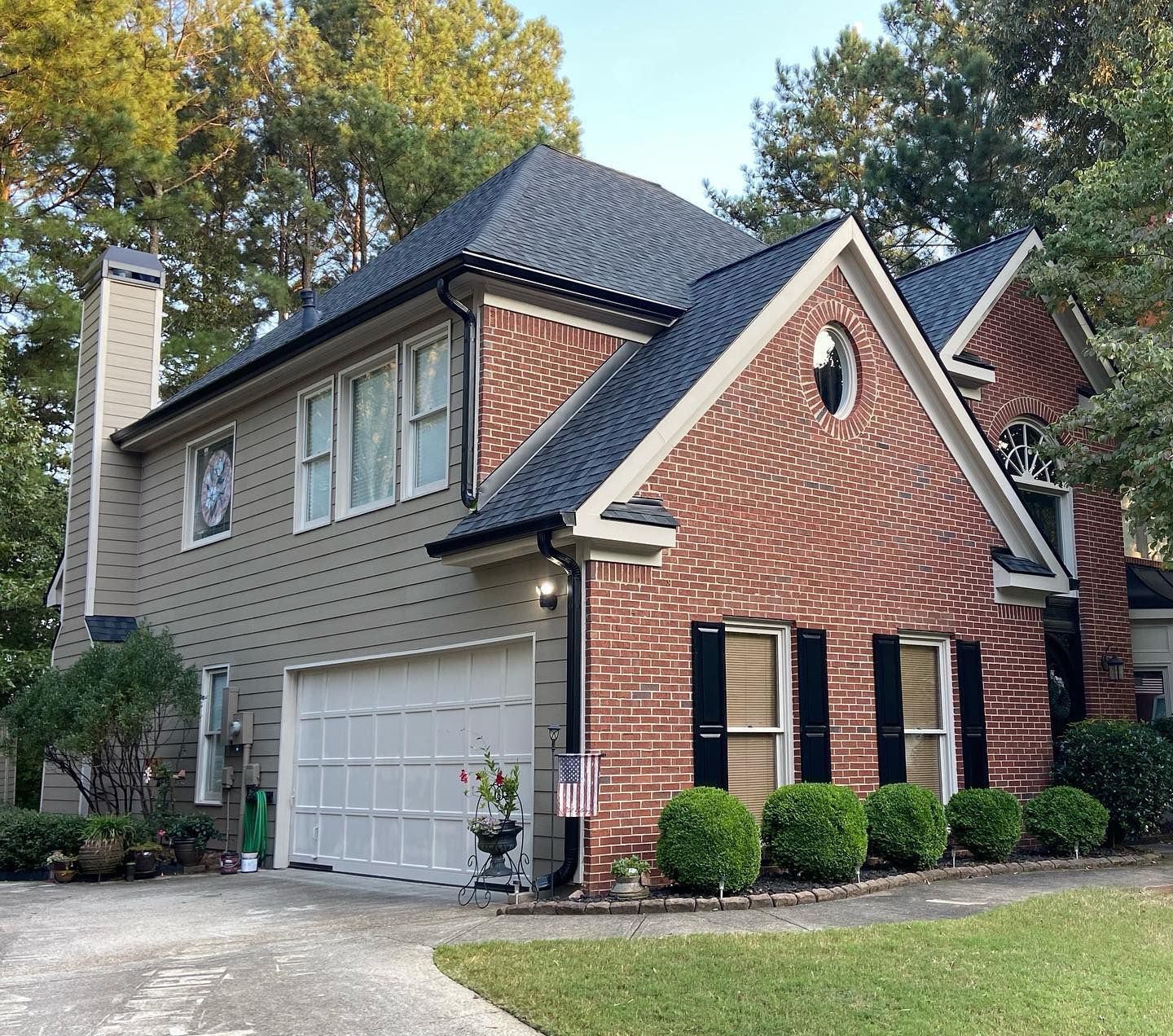 Two-story house with brick and siding, dark roof, white garage door, and black shutters.