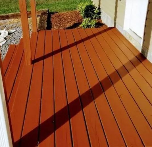 Brown wooden deck with shadow, steps leading down to green grass.