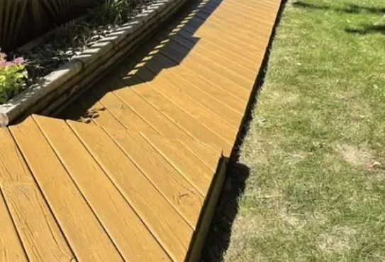 Wooden walkway alongside a garden bed and grass lawn.