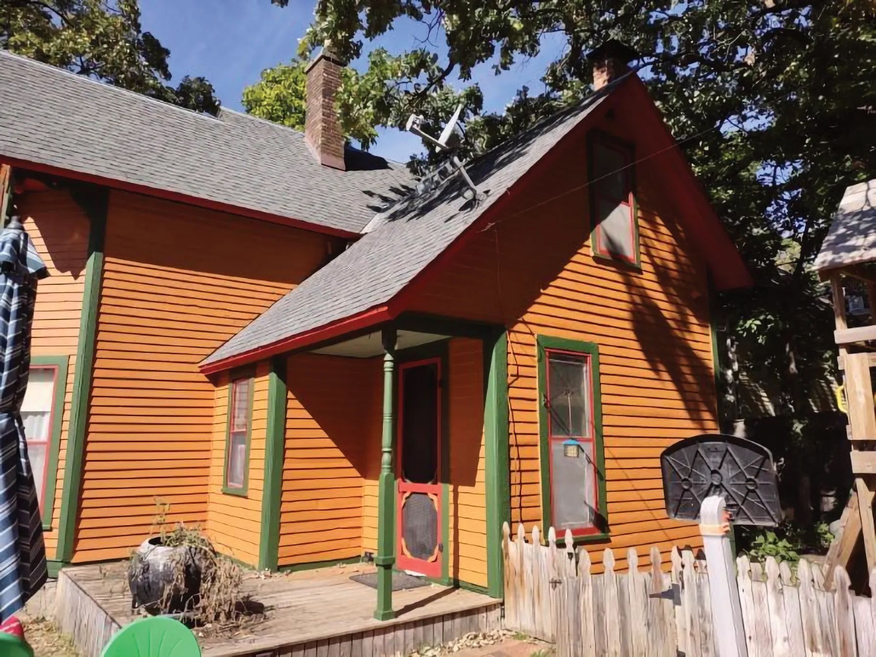 Orange house with red trim, green accents, and a small porch; a fenced yard.