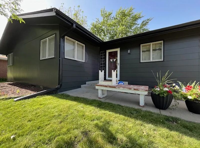 Black house with white trim, steps, bench, flowerpots, and green lawn on a sunny day.