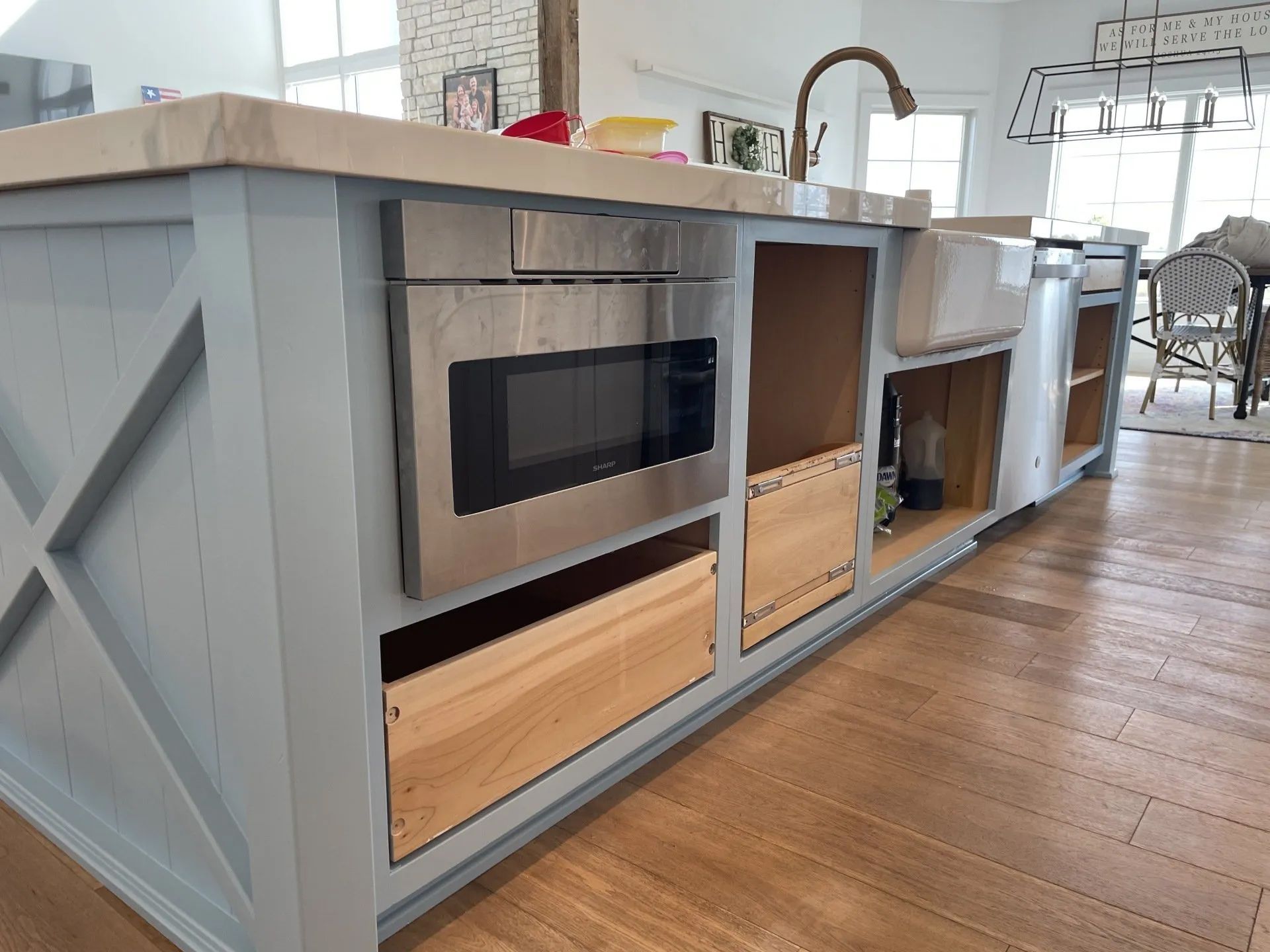 Kitchen island with built-in microwave and cabinetry. Light blue cabinets, wooden interior with light wood flooring.