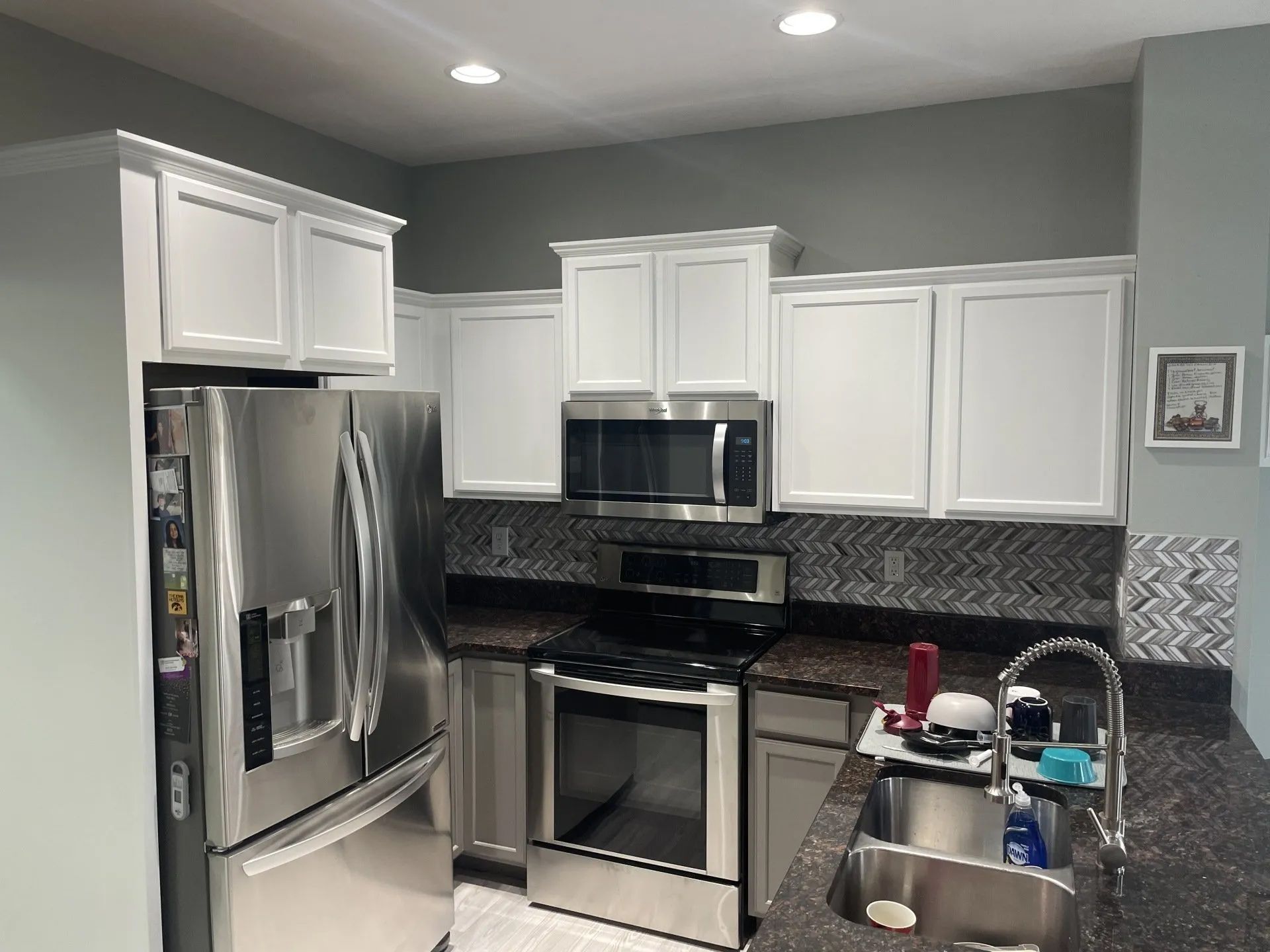White kitchen cabinets, stainless steel appliances, dark countertops, and a gray wall.