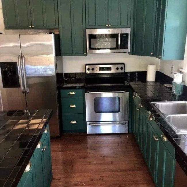 Green kitchen cabinets with black countertops and stainless steel appliances.