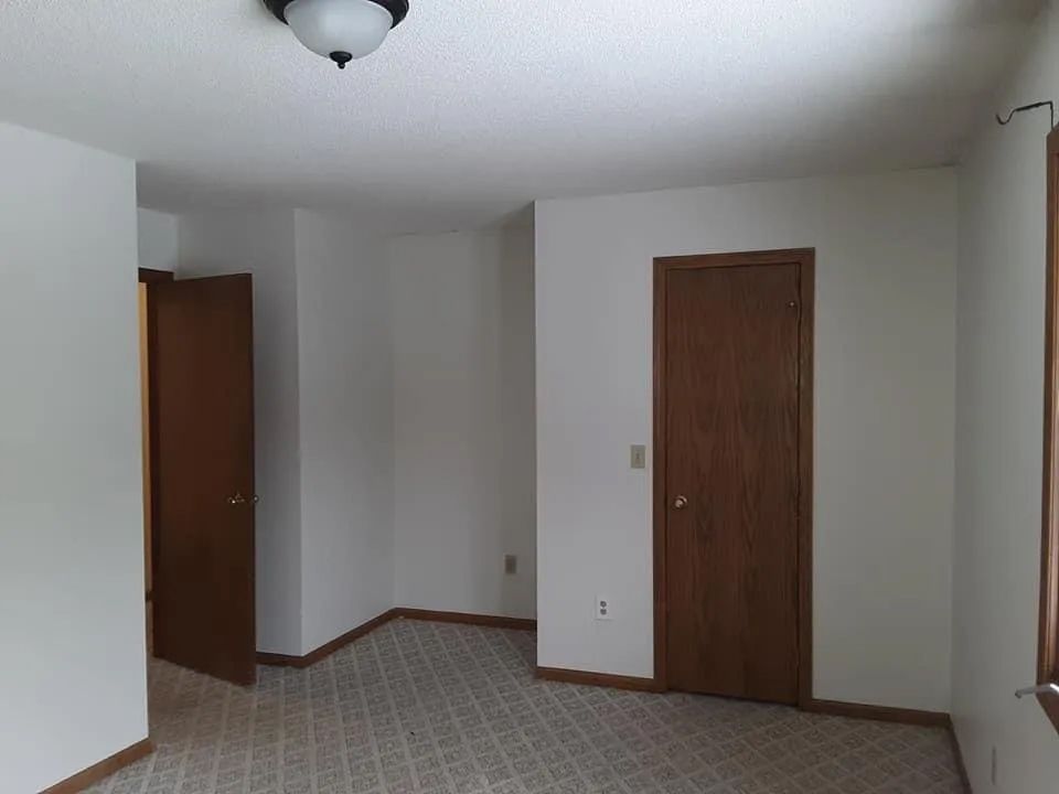 Empty room with white walls, brown doors, and patterned carpet.