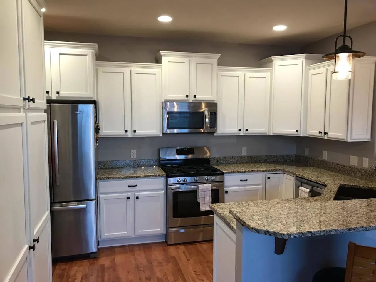 White kitchen with stainless steel appliances, granite countertops, and wood floors.