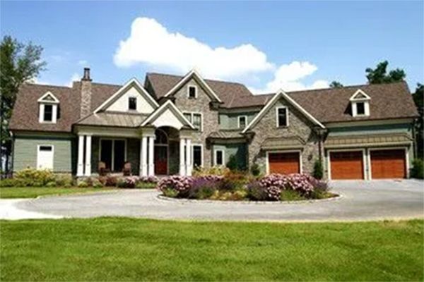 Large, multi-level home with a circular driveway and landscaping under a blue sky.