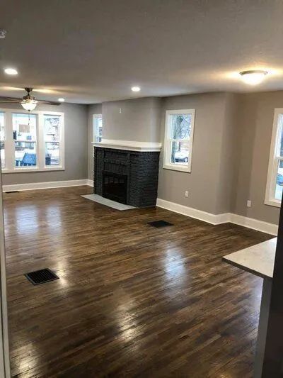 A living room with dark wood floors, gray walls, fireplace, windows, and recessed lighting.