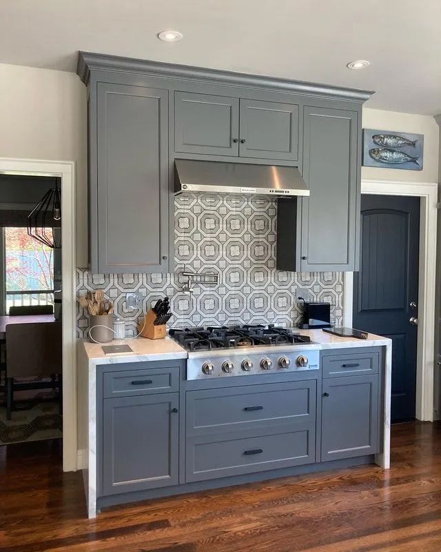 Gray kitchen cabinets with stovetop, tile backsplash, and stainless steel hood.