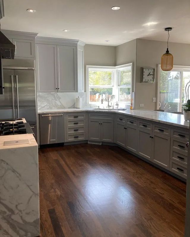 Modern kitchen with gray cabinets, marble countertops, stainless steel appliances, and dark wood floors.