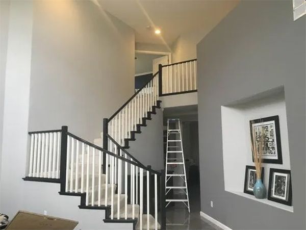 Two-story home interior with a staircase and gray walls. Black and white railing. Ladder in center. Art on right wall.