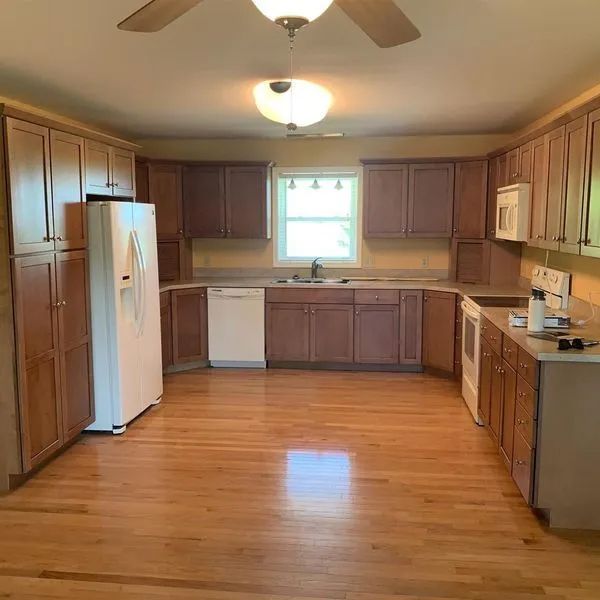 Kitchen with wooden cabinets and flooring, white appliances, and yellow walls.