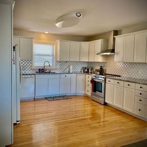 Bright kitchen with white cabinets, stainless steel appliances, and hardwood floors.