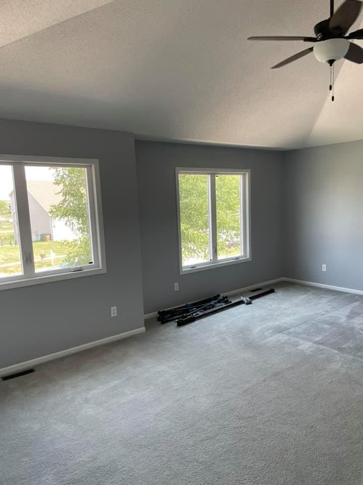 Spacious room with gray walls, white-framed windows, and gray carpet. Black objects lie on the floor.